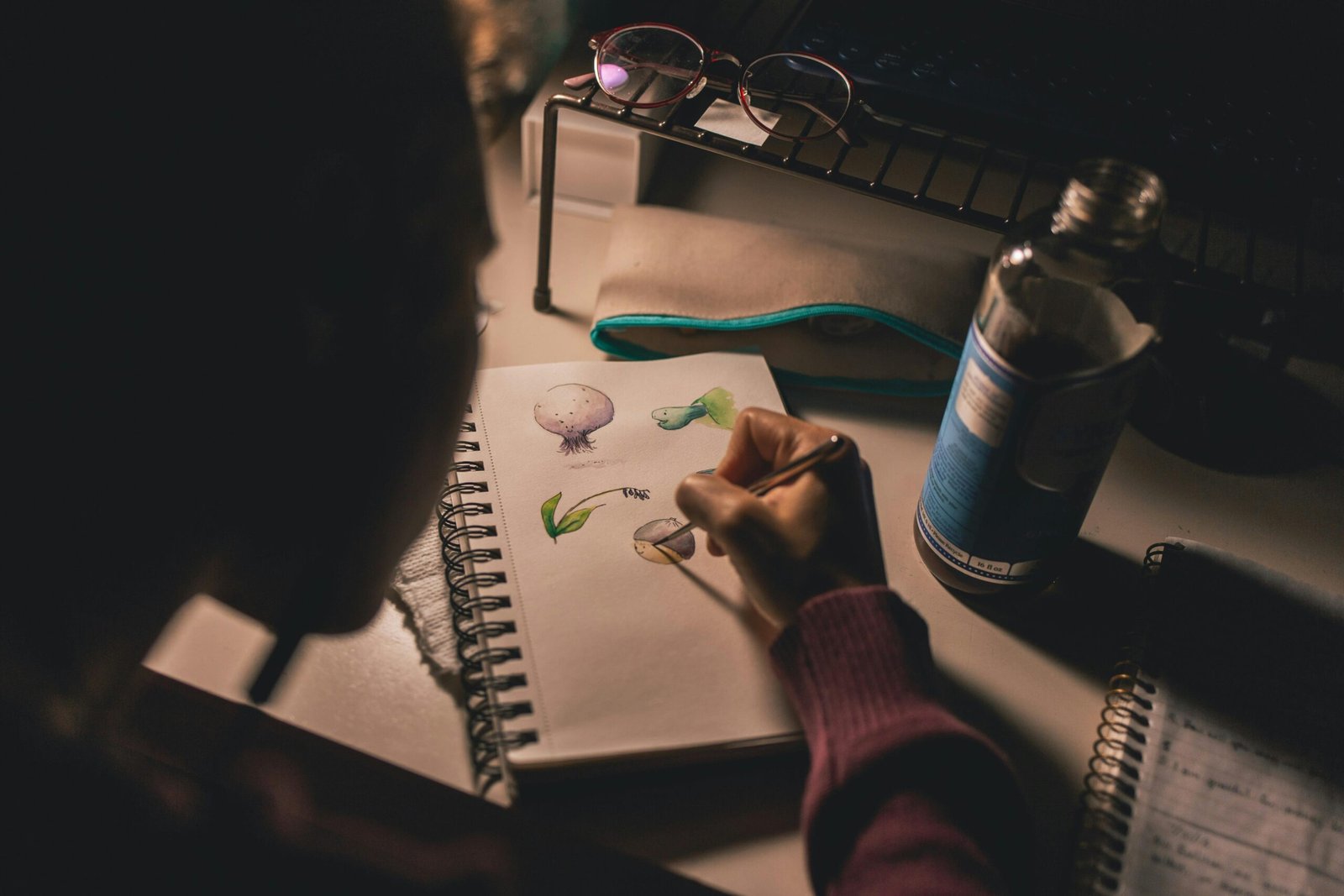 An artist sketches on a notebook under soft lighting, focusing on creativity and inspiration.